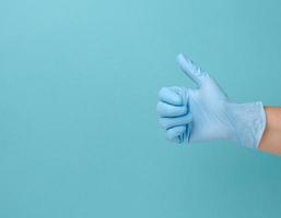 Hand in einem blauen medizinischen Einweghandschuh aus Latex zeigt die Geste wie auf blauem Hintergrund foto