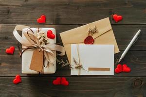 geschenkbox und grußkarte mit schleifenband und papierherzen auf holztisch zum valentinstag. Platz kopieren. foto
