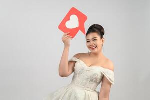 asiatische schöne Braut, die mit Herzzeichen auf weißem Hintergrund lächelt und aufwirft foto