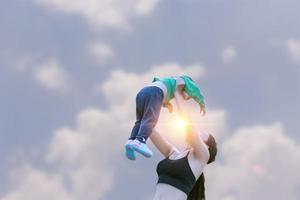 Porträt einer Mutter, die eine glückliche Tochter mit Händen hält, die mit weißen Wolken auf der Natur spazieren gehen. Familien verbringen gemeinsam Zeit im Urlaub. foto