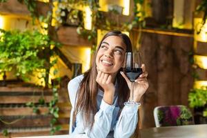 Bild einer süßen, hübschen jungen Frau, die im Café sitzt und ein Glas hält und Wein trinkt. Porträt einer schönen Weinverkostungstouristenfrau. foto