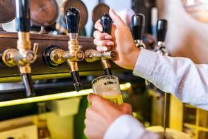 Hand des Barkeepers, der ein großes Lagerbier in den Zapfhahn gießt. helles und modernes neonlicht, frauenhände. Bier für den Kunden einschenken. foto
