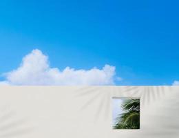 wandbetonstruktur mit offenem fenster und kokospalmenblättern gegen blauen himmel und wolken, äußeres weißes zementgebäude, moderne architektur mit quadratischem rahmen im frühlings- oder sommerhimmel foto