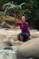 asiatische Frau, die mit schmutzigem Wasser aus einem schmutzigen Fluss spielt, während sie ein lila Kleid und einen grünen Rock trägt foto