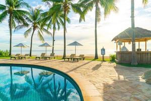 Wunderschöner Luxus-Sonnenschirm und -Stuhl um den Außenpool im Hotel und Resort mit Kokospalme bei Sonnenuntergang oder Sonnenaufgang foto