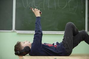 Das Kind ruht sich in der Schule aus. ein schuljunge liegt in kopfhörern auf einer schulbank und schaut in ein smartphone.wechsel in der schule. foto