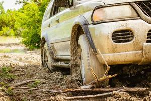 Nahaufnahme Vorderrad des 4WD-Fahrzeugs, das im Schlamm steckt, gehen Sie rückwärts vorwärts und verwenden Sie den Baumzweig im Freien in der wwt-Frühlingsnatur. extreme straßenbedingungen im sommer nach dem regenkonzept foto