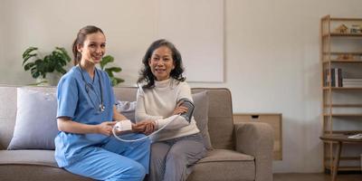 glückliche Seniorin, die ihren Blutdruck in einem Pflegeheim von ihrer Pflegekraft messen lässt. Glückliche Krankenschwester, die den Blutdruck einer älteren Frau im Wohnzimmer misst foto