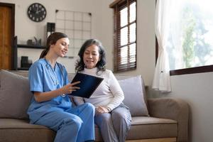 asiatische krankenschwester, die großmutter den gesundheitsuntersuchungsbericht zeigt und tipps gibt. medizinisch betreutes leben besuchen seniorenpatienten zu hause. konzept für häusliche krankenpflege und gesundheitspflege foto