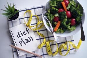 Konzept für gesunde Ernährung. Gemüsesalat, Notizbuch zur Lebensmittelkontrolle und Maßband foto