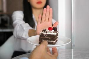 Eines der Mädchen aus dem Gesundheitswesen schob mit der Hand einen Teller mit Schokoladenkuchen. weigern Sie sich, Lebensmittel zu essen, die Transfette enthalten. foto