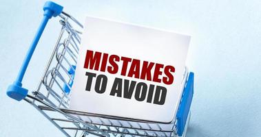 Einkaufswagen- und Textfehler, die auf der Whitepaper-Notizliste zu vermeiden sind. Einkaufsliste Konzept auf blauem Hintergrund. foto