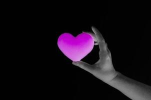 Frauenhand, die leeres purpurrotes Herz auf dunklem Hintergrund, Symbol der bisexuellen Liebe oder Verabredung hält foto