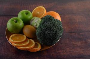 Orangenscheiben mit Apfel, Kiwi und Brokkoli auf einem Holzteller foto