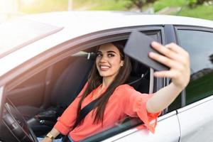 lächelnde junge frau, die selfie-foto mit smartphone-kamera draußen im auto macht. Urlaubs- und Tourismuskonzept - lächelndes Teenager-Mädchen, das im Auto ein Selfie-Foto mit Smartphone-Kamera im Freien macht foto