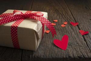 geschenkbox mit rotem schleifenband und papierherz auf hintergrund für valentinstag. foto