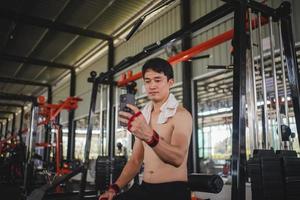 asiatische männer, die nach dem training im fitnessstudio handys für selfies verwenden foto