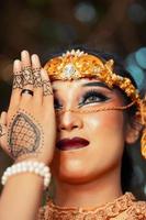 asiatische Frau mit Make-up, die sein Gesicht mit ihrer Hand bedeckt, während sie geschminkt ist und eine goldene Krone und eine goldene Tiara trägt foto