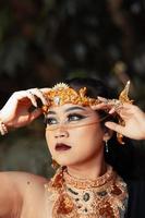 Schöne exotische Frau mit goldenem Kopfschmuck und goldener Halskette am Körper, während sie Make-up trägt foto
