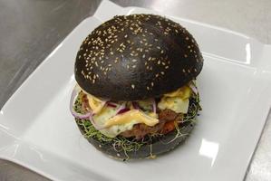 schwarzer Burger auf einem weißen Teller servierfertig foto