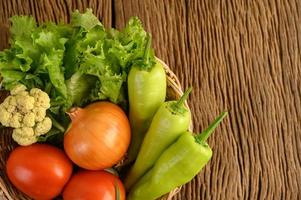 Paprika, Tomate, Zwiebel, Salat und Blumenkohl auf einem Holzkorb auf einem Holztisch foto