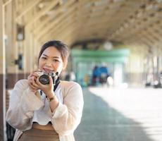 yong mädchen asiatische frau schöne coole lange haare tragen weißes hemd modell mit retro-filmkamera am bahnhof bangkok stehen, reisen im urlaub während des abendtages foto