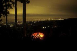 Sonnenuntergang in der Stadt. stadtlichtansicht von der spitze des berges. Campingplatz Zelt in der dunklen Nacht foto