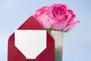 Roter Umschlag mit Platz für Text und Vase mit rosa Rosen auf blauem Hintergrund. einladung, geburtstag, 8. märz, internationaler frauentag, muttertag. Platz kopieren foto