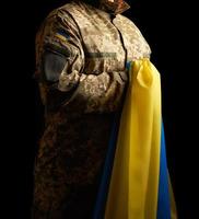 Der ukrainische Soldat hält die gelb-blaue Flagge des Staates in der Hand, er drückte seine Hand auf seine Brust foto