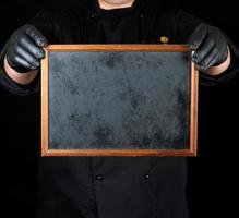 koch in schwarzer uniform und schwarzen latexhandschuhen hält einen leeren holzrahmen foto