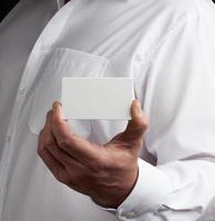 Die männliche Hand hält eine rechteckige, leere Visitenkarte aus weißem Papier foto