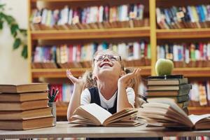 glücklich fühlen. süßes kleines Mädchen mit Zöpfen ist in der Bibliothek. Apfel auf die Bücher foto