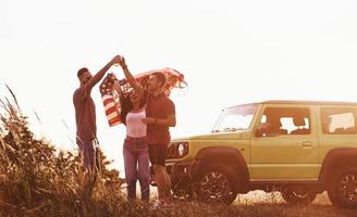 Gespräch haben. freunde haben ein schönes wochenende im freien in der nähe ihres grünen autos mit usa-flagge foto