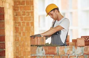 ziegel einbau. junger mann, der tagsüber in uniform auf dem bau arbeitet foto