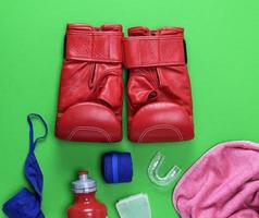 rote Boxhandschuhe aus Leder, eine Plastikwasserflasche und ein rosa Handtuch und eine blaue Textilbandage foto