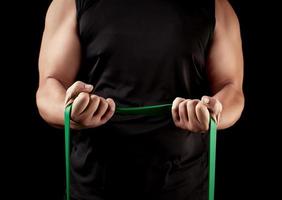 athlet mit einem muskulösen körper in schwarzer kleidung macht körperliche übungen mit grünem gummi foto