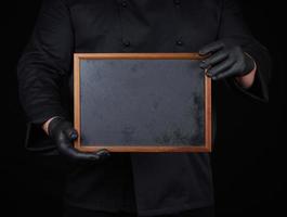 Koch in schwarzer Uniform hält einen leeren Holzrahmen foto