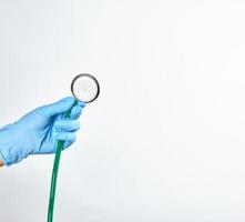 blaue sterile behandschuhte hand, die ein grünes medizinisches stethoskop hält foto