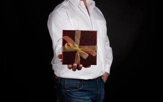 erwachsener mann in einem weißen hemd hält eine rote quadratische schachtel mit einer geknoteten goldenen schleife foto
