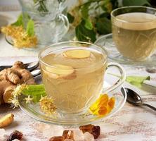 transparente Tasse Kräuterlindentee und Ingwerstücke auf einem weißen Holzbrett foto