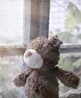 Brauner Teddybär sitzt auf einer Fensterbank und schaut aus dem Fenster foto