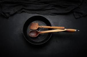 leere runde gusseiserne Bratpfanne mit Holzgriff auf schwarzem Tisch, Draufsicht foto