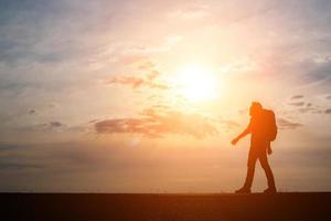 Schattenbild eines jungen Rucksacktouristenmannes, der während des Sonnenuntergangs geht foto