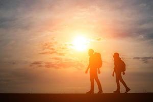 Silhouetten von zwei Wanderern mit Rucksäcken, die den Sonnenuntergang genießen