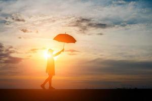 Silhouette einer Frau, die einen Regenschirm am Strand und am Sonnenuntergang hält foto