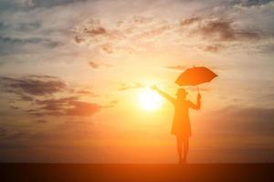 Silhouette einer Frau, die einen Regenschirm am Strand und am Sonnenuntergang hält foto