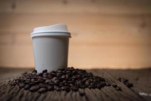 Papierkaffeetasse mit Kaffeebohnen auf einem Holztisch