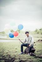 junger Mann, der bunte Luftballons in der Natur hält foto