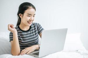 eine junge Frau spielt auf ihrem Laptop im Bett foto
