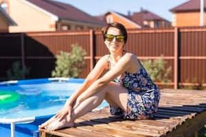 Porträt einer hübschen jungen Frau im Pyjama, die in der Nähe eines aufblasbaren Swimmingpools sitzt - Sommer- und Landlebenskonzept foto
